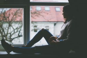 A woman is sitting in the window. She is experiencing disenfranchised grief.