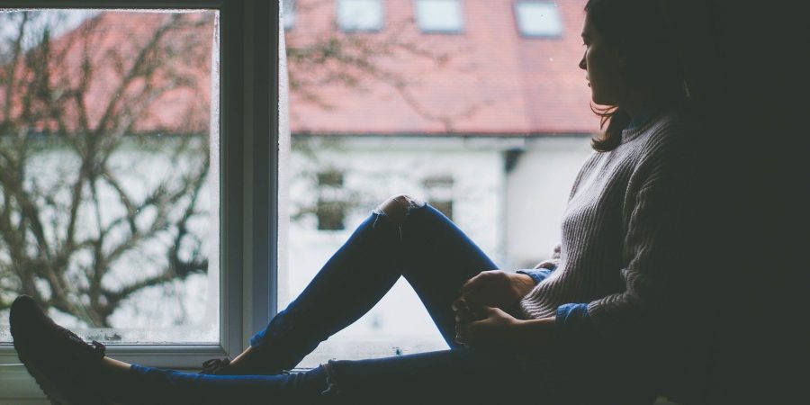 A woman is sitting in the window. She is experiencing disenfranchised grief.